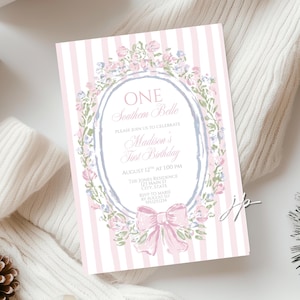Puede incluir: Una tarjeta de invitación a rayas rosas y blancas con detalles florales y lazo. El texto dice "ONE Southern Belle" y "Madison's First Birthday". La tarjeta incluye detalles del evento y está diseñada para una celebración de primer cumpleaños.