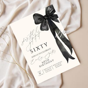 Może przedstawiać: Kremowe zaproszenie z czarną akwarelową kokardą i wstążką. Tekst brzmi "She's still got it at SIXTY" i zaprasza gości na obchody 60. urodzin Emily Smith 18 czerwca.