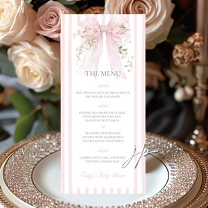 Könnte beinhalten: Eine Menükarte mit rosa und weißen Streifen, verziert mit einer Aquarellschleife und floralen Akzenten. Der Text "THE MENU" steht oben, darunter sind die Menüpunkte aufgeführt. Die Karte liegt auf einem dekorativen Teller.