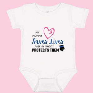 May include: White baby bodysuit with the text "My Mommy Saves Lives and my Daddy Protects Them". The design includes a pink heart with a ribbon, and a blue police badge. The bodysuit is made of soft material.