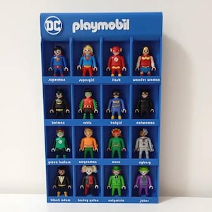 Può includere: Una vetrina blu Playmobil con personaggi DC Comics. Le figure includono Superman, Supergirl, Flash, Wonder Woman, Batman, Robin, Batgirl, Catwoman, Green Lantern, Aquaman, Mera, Cyborg, Black Adam, Harley Quinn, Enigmista e Joker.