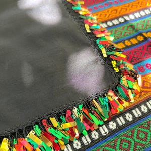 May include: A black textile with a colorful sequined fringe. The fringe features red, green, gold, and pink sequins. The textile is set against a vibrant, patterned background with stripes and geometric designs.