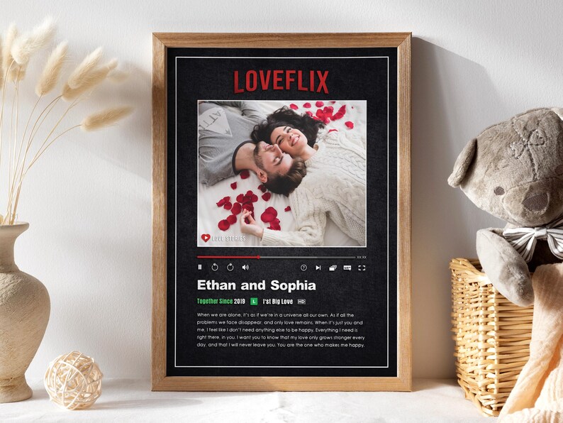 May include: A framed print with a black background and a red "LOVEFLIX" logo. The print features a photo of a couple lying on a bed of rose petals. The text below the photo reads "Ethan and Sophia" and includes a quote about their love.
