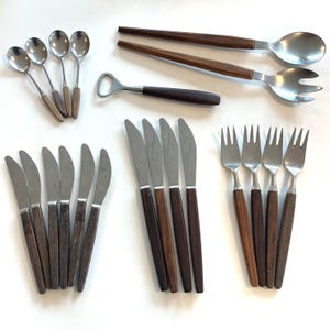 Könnte beinhalten: Eine Sammlung von Vintage-Besteck mit Edelstahl und Holzgriffen. Enthält Löffel, Salatgabeln, Messer und Servierlöffel. Die Holzgriffe haben eine dunkelbraune Oberfläche. Ein Flaschenöffner mit dunkelbraunem Griff ist ebenfalls enthalten.