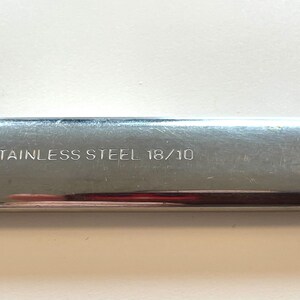 May include: Close-up of a stainless steel utensil with the text "STAINLESS STEEL 18/10" etched on the surface. The utensil has a shiny, reflective surface.