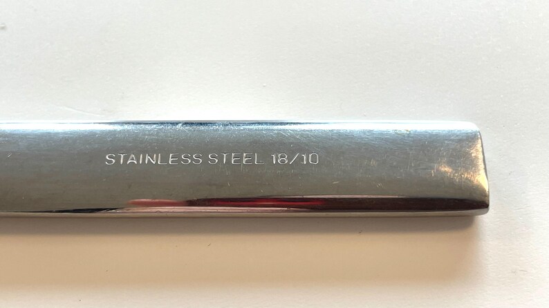 May include: Close-up of a stainless steel utensil with the text "STAINLESS STEEL 18/10" etched on the surface. The utensil has a shiny, reflective surface.