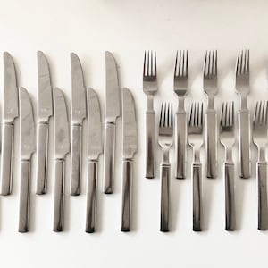 May include: A set of 12 silver-toned forks and 12 silver-toned knives. The forks and knives are arranged in two rows, with the forks on top and the knives on the bottom.