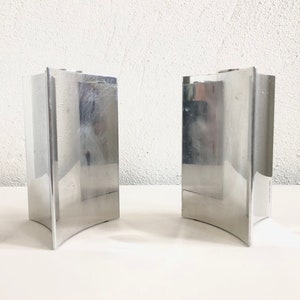 Puede incluir: Dos candelabros de metal plateado con base curva. Los candelabros son altos y rectangulares.