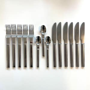 May include: A set of stainless steel flatware, including forks, spoons, and knives, arranged on a white surface. The silverware has a simple, modern design with rectangular handles and a polished finish. The set includes forks, spoons, and knives.