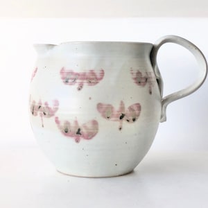 May include: White ceramic pitcher with a handle and a pink floral design.