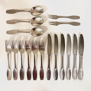 May include: A collection of stainless steel flatware, including spoons, forks, and knives, arranged on a white surface. The spoons have oval bowls, while the forks and knives have elongated handles.
