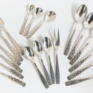以下が含まれることがあります： フォーク、スプーン、サービングフォークを含む、銀色のカトラリーの詰め合わせ。ハンドルはダイヤモンドのようなテクスチャパターンで、スプーンのボウルとフォークの歯は滑らかで反射性があります。白い表面に配置されています。