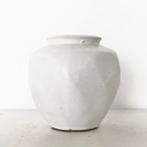 May include: White ceramic vase with a rounded, slightly textured body. The vase has a simple, elegant design.