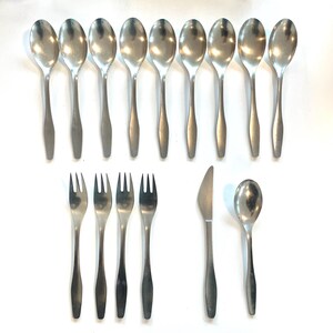 May include: A set of stainless steel flatware, including spoons, forks, a knife, and a serving spoon. The spoons have oval bowls and long, slender handles. The forks have three tines. The knife has a curved blade.
