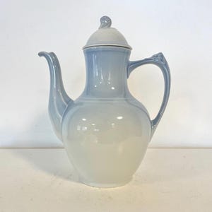 Peut inclure: Une cafetière en porcelaine bleu clair et blanche avec un couvercle et une anse incurvée. Le bec verseur est incurvé et le couvercle a un petit bouton décoratif. Le pot a une finition brillante et est probablement vintage.