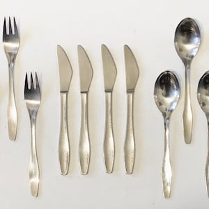 Könnte beinhalten: Ein Set aus Edelstahlbesteck, darunter Gabeln, Messer und Löffel. Die Gabeln haben drei Zinken, die Messer haben eine abgerundete Spitze und die Löffel haben eine ovale Schale. Das Besteck ist auf einer weißen Oberfläche angeordnet.