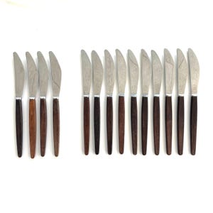 May include: A collection of vintage stainless steel knives with wooden handles. The knives are arranged in two groups, with a variety of dark brown and medium brown handles. The blades are silver and have a serrated edge.