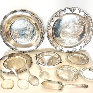 Pode incluir: Uma coleção de travessas e utensílios de servir de prata antigas. O conjunto inclui travessas grandes, pratos pequenos e colheres de servir. As peças têm bordas ornamentadas e decorativas.