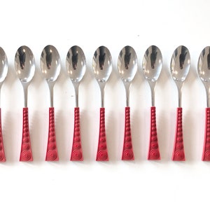 May include: Eight stainless steel spoons with red handles. The spoons have a polished, reflective surface and a teardrop-shaped bowl. The red handles feature a geometric design with circular and vertical patterns, adding a decorative touch to the silverware.