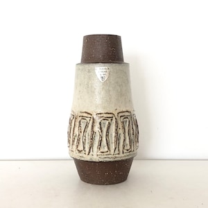 Puede incluir: Un jarrón de cerámica blanca con diseños geométricos marrones. El jarrón tiene un borde y una base marrones. El jarrón está marcado con una pegatina plateada que dice "Rosenthal Selb Germany".