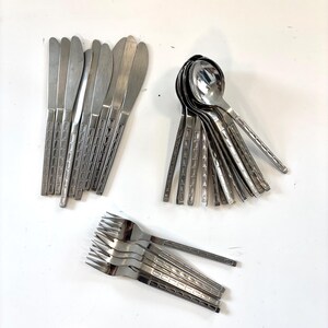 May include: A collection of stainless steel flatware including several knives, spoons, and forks. Each piece features a polished finish and a distinct handle design with a series of rectangular indentations arranged in a vertical grid pattern.