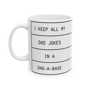 May include: White ceramic mug with the text "I KEEP ALL MY DAD JOKES IN A DAD-A-BASE" in black block letters. The mug has a white handle and a cylindrical shape.