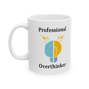 May include: White ceramic mug with the words "Professional Overthinker" in black. The mug features a graphic of a brain and a lightbulb, split in half, with yellow lightning bolts above.