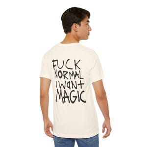 Puede incluir: Camiseta color crema con el texto "FUCK NORMAL I WANT MAGIC" en negro, con letras manuscritas. La camiseta es de manga corta y cuello redondo.