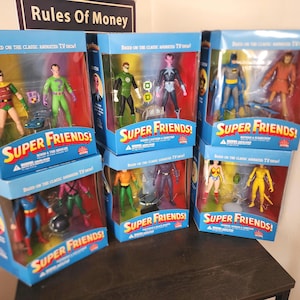 Może przedstawiać: Kolekcja zapakowanych figurek Super Friends. Niebieskie pudełka z logo Super Friends i wizerunkami postaci. Figurki obejmują Batmana, Supermana, Wonder Woman i innych. Widoczny tekst "Based on the Classic Animated TV Show".
