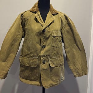 May include: A brown canvas jacket with a corduroy collar and multiple pockets. The jacket has a button closure and is a classic style.