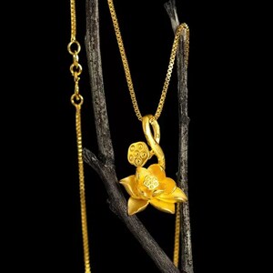 May include: A gold chain necklace with a lotus flower pendant. The pendant is detailed with a stem and seed pods.