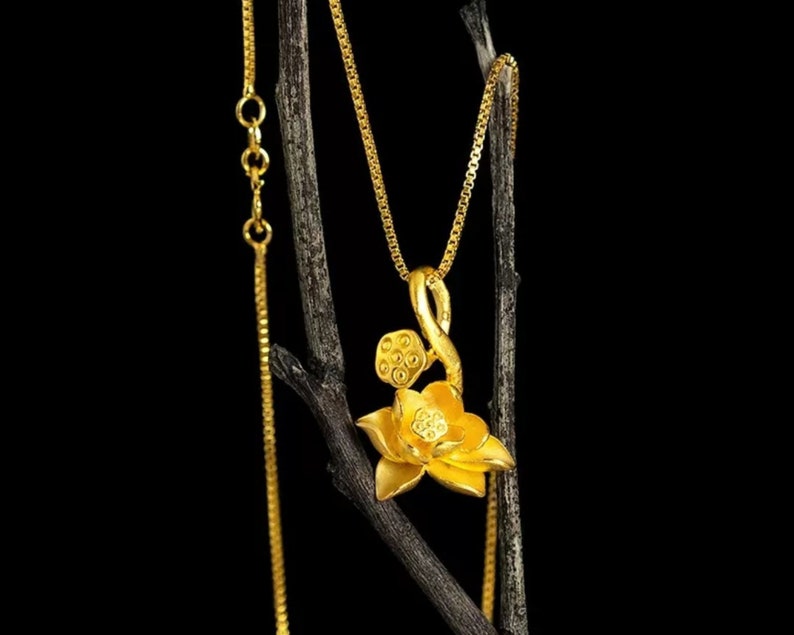 May include: A gold chain necklace with a lotus flower pendant. The pendant is detailed with a stem and seed pods.