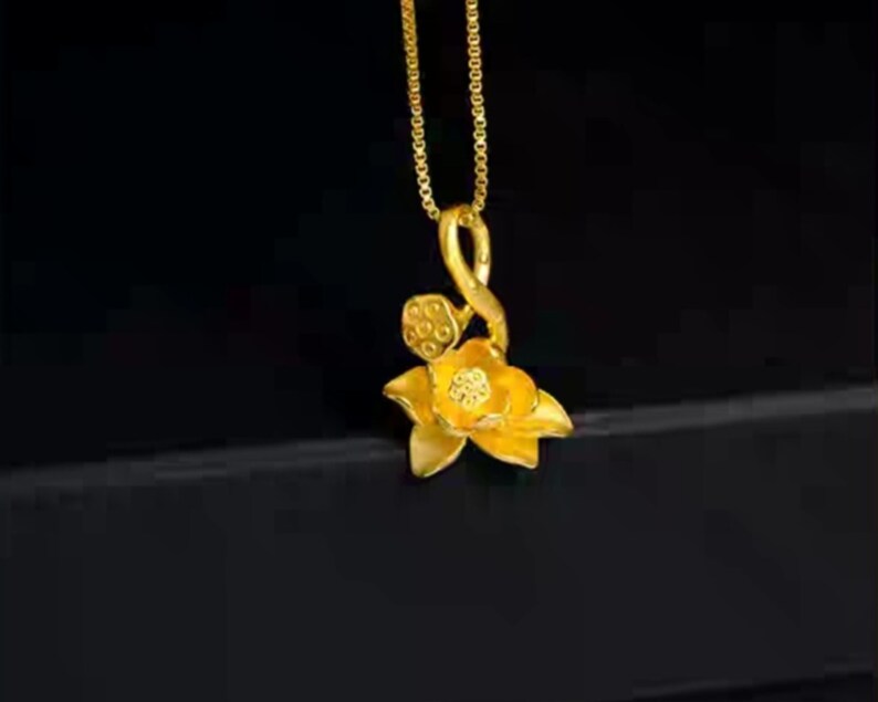 May include: A gold necklace with a pendant shaped like a lotus flower. The pendant is detailed with a stem and leaves.