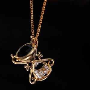 May include: A gold-tone necklace featuring a black and clear hourglass pendant with clear rhinestones.