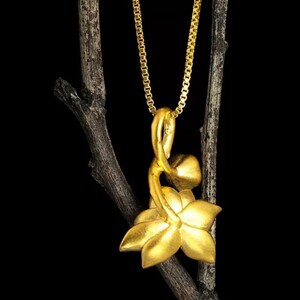 May include: A gold pendant necklace featuring a stylized flower design. The pendant is shaped like a flower with a stem and leaves. The necklace is on a gold chain.