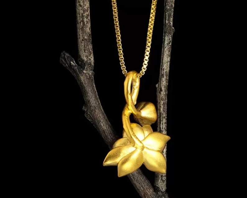May include: A gold pendant necklace featuring a stylized flower design. The pendant is shaped like a flower with a stem and leaves. The necklace is on a gold chain.