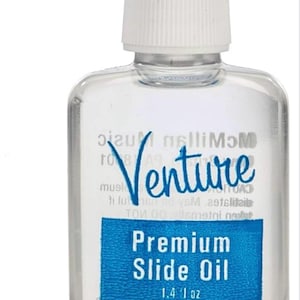 May include: Clear plastic bottle of Venture Premium Slide Oil with a white cap. The label is blue with white text that reads "Premium Slide Oil" and "1.4 fl oz". The word "Venture" is written in blue cursive.