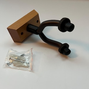 May include: A guitar wall mount with a wooden base and a dark bronze-colored yoke. The yoke has two black rubber supports. A small bag of mounting hardware is included.