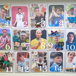 May include: A collection of fifteen rectangular trading cards featuring various soccer players, each decorated with colorful stickers, glittery letter accents, and numbered labels from 1 to 15. The cards are encased in clear protective plastic sleeves.