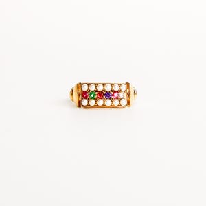 Op de afbeelding: Een gouden ring met een rechthoekig voorvlak bezet met twee horizontale rijen kleine witte parels. Tussen de parelrijen bevindt zich een centrale lijn van vier ronde gefacetteerde edelstenen in groen, rood, paars en roze in een gouden band.