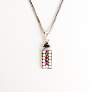 May include: A silver-toned necklace featuring a rectangular pendant suspended from a box chain. The pendant is bordered by small white pearls and contains a vertical row of five colourful round gemstones in pink, green, red, purple, and clear.