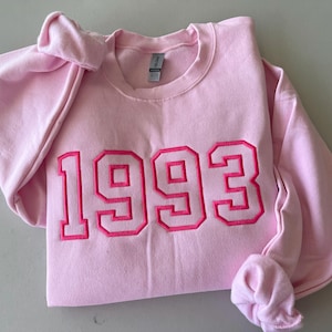 May include: Pink sweatshirt with the year 1993 embroidered in pink on the front.