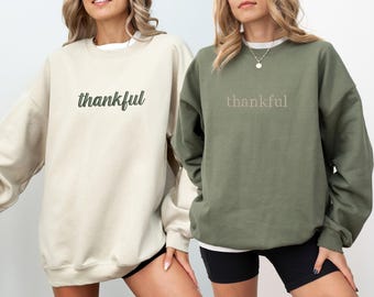 May include: Two sweatshirts with the word "thankful" printed on them. One sweatshirt is beige and the other is olive green.
