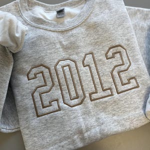 May include: A gray sweatshirt with the year 2012 embroidered in brown on the front.