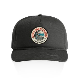 May include: A charcoal gray baseball cap featuring a circular embroidered patch on the front. The patch displays a coastal scene with the text CITY OF SAN CLEMENTE, CALIFORNIA, 1928, and SPANISH VILLAGE in red, black, and blue thread colors.