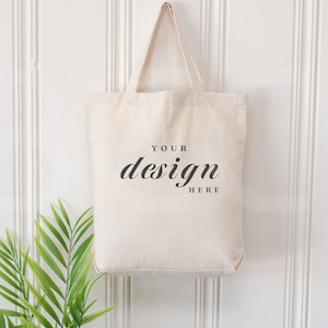 Könnte beinhalten: Eine schlichte weiße Canvas-Tragetasche mit dem Aufdruck "YOUR design HERE" in Schwarz auf der Vorderseite.