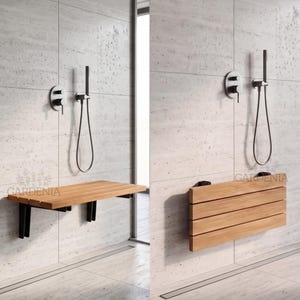 Peut inclure: Un siège de douche mural composé de lattes en bois brun clair horizontal et de supports en métal noir. Le siège est présenté en position horizontale déployée et en position verticale repliée contre un mur de douche en carrelage gris clair.