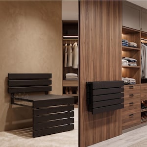 Op de afbeelding: Een donkerbruine, aan de muur gemonteerde opklapbank met een lattenontwerp. De bank wordt getoond in zowel de opgevouwen als de uitgevouwen positie, gemonteerd aan een muur. Het ontwerp is minimalistisch en modern.