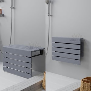 Peut inclure: Un banc de douche pliable fixé au mur, doté d'un design à lattes gris clair avec des supports en métal noir. Le banc est présenté en position horizontale étendue et en position verticale repliée contre un mur avec le texte GARDENIA.