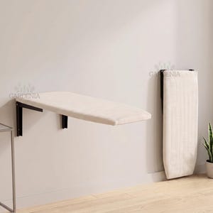 Peut inclure: Une planche à repasser murale pliable avec une housse en tissu crème et des supports métalliques noirs. L'unité est présentée en position horizontale étendue et en position verticale repliée, avec le texte GARDENIA visible.